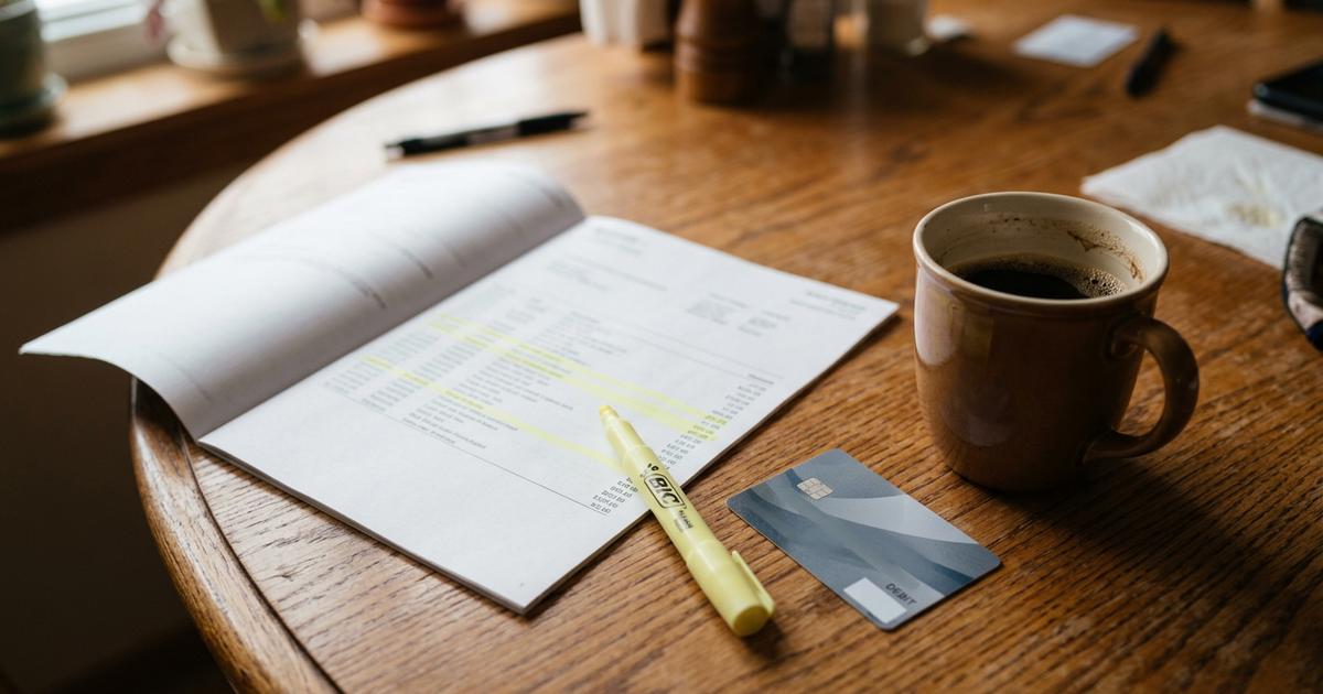 A printed bank statement on a table with a highlighter and a debit card